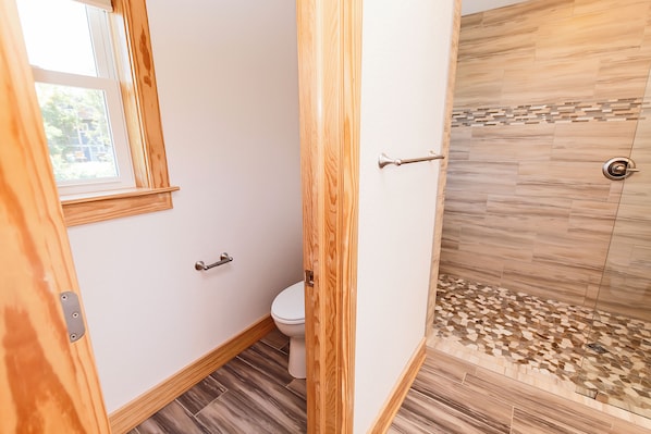 A bathroom with a toilet, a shower with mosaic tiles, and wooden trim.