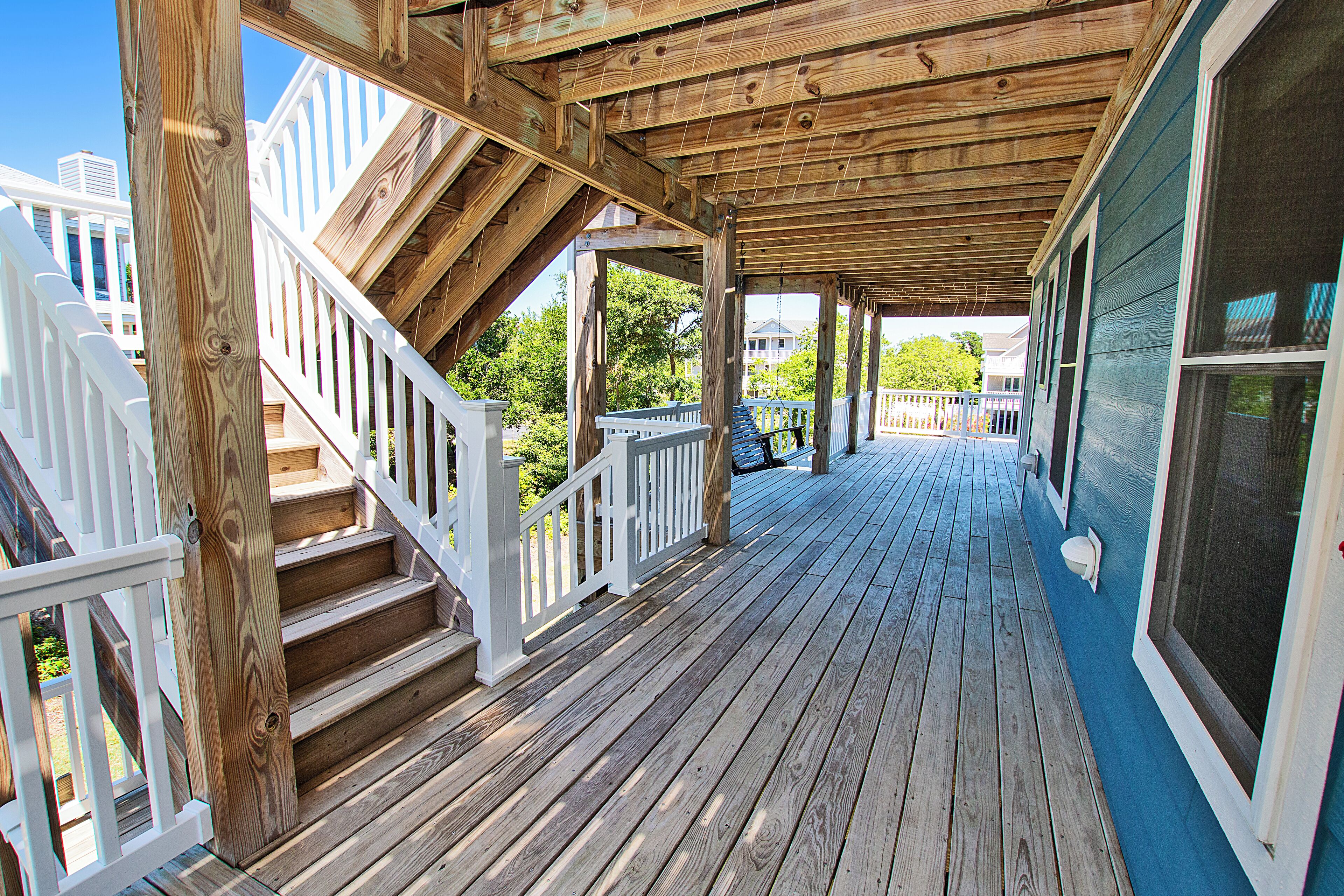 Um deck de madeira com guarda-corpo branco, uma escadaria e vista para uma área residencial.