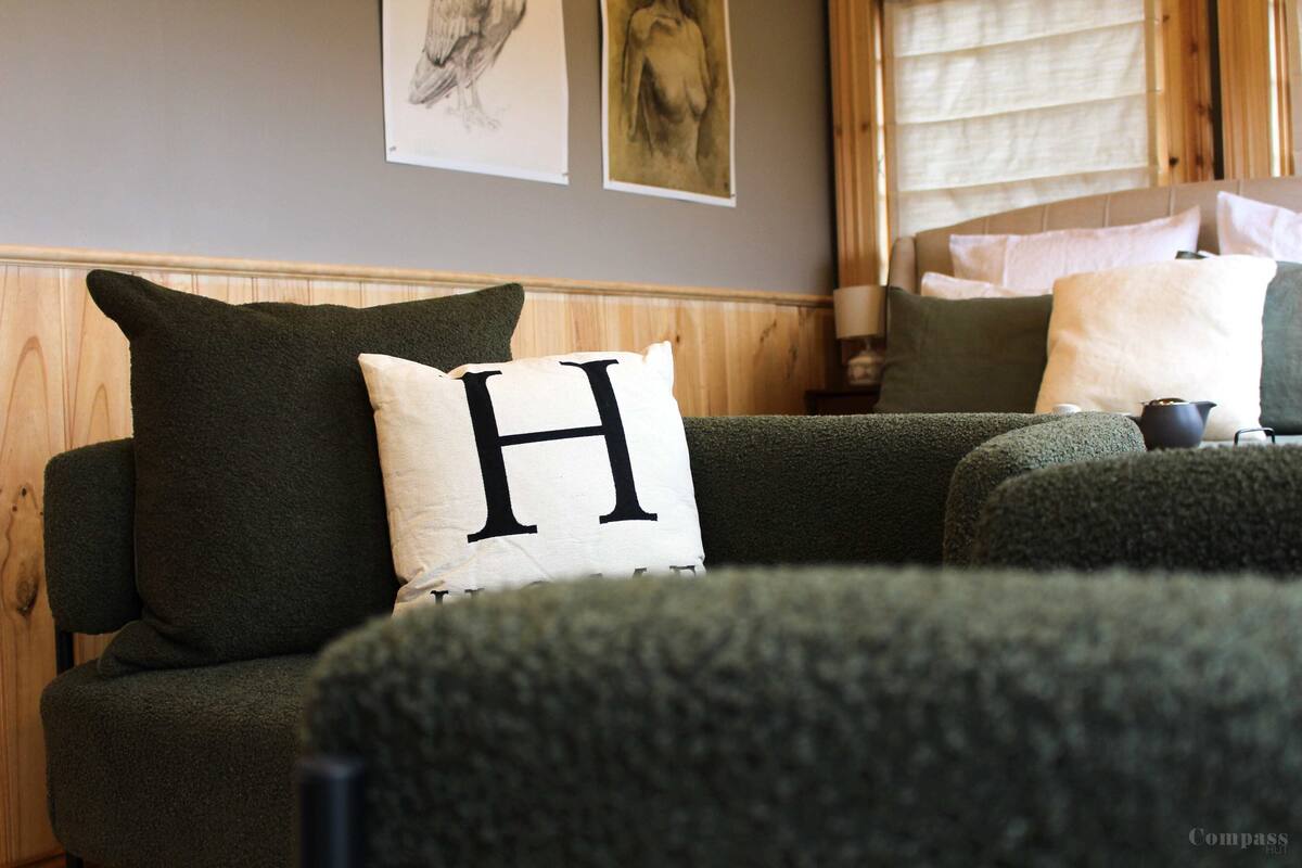 Un salon chaleureux avec un canapé vert, un coussin blanc orné d’un « H » noir et des lambris en bois sur les murs.