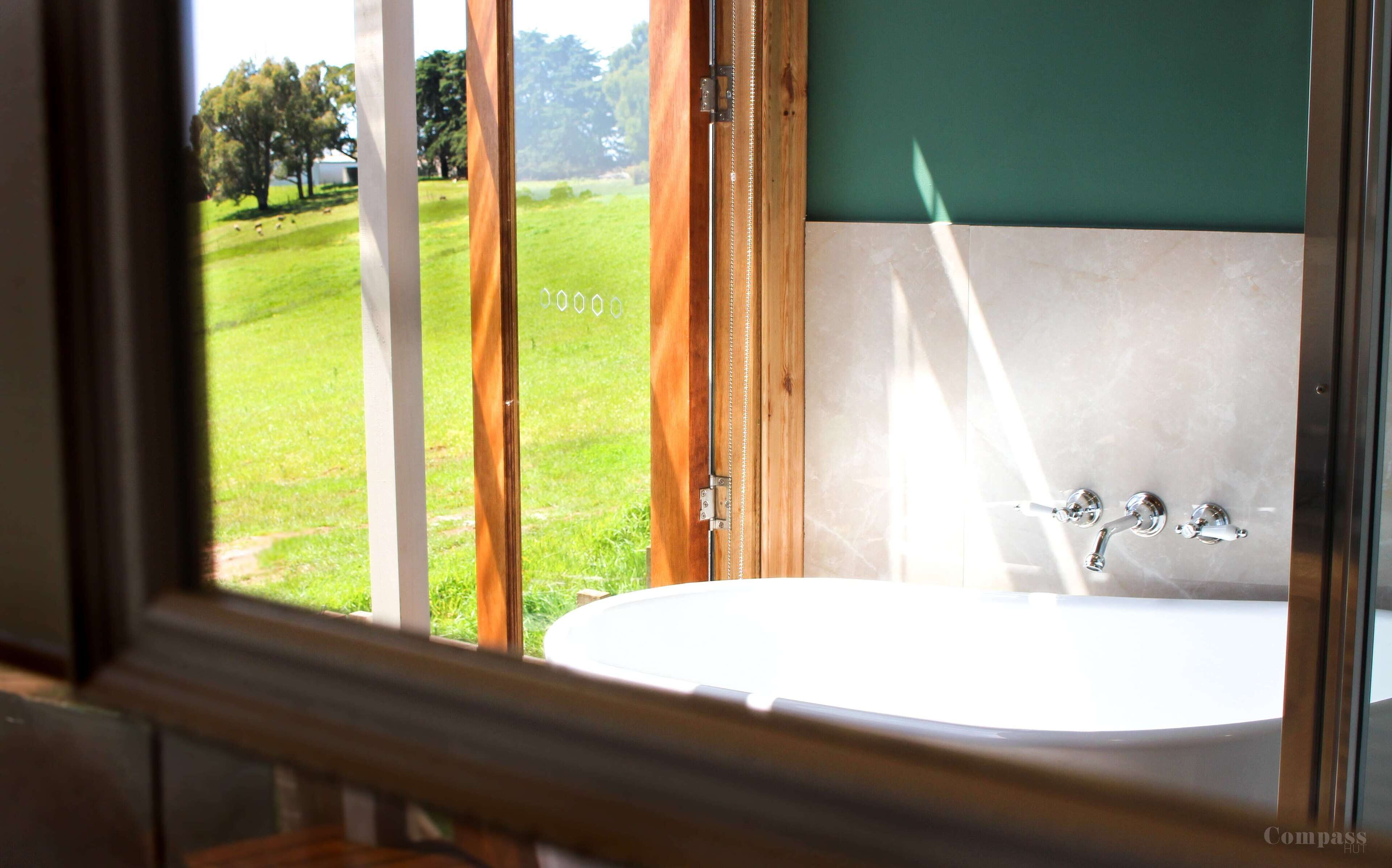 Um banheiro com uma banheira grande, vista para um gramado verde e moldura de porta de madeira.