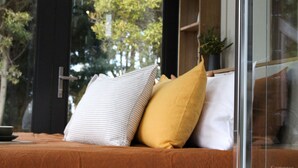 Un lit avec un oreiller à rayures et un oreiller jaune, une fenêtre donnant sur des arbres et une plante posée sur le rebord de la fenêtre.