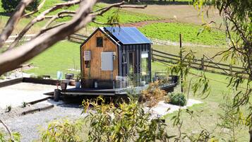 Une cabane en bois surmontée d’un toit équipé de panneaux solaires, entourée d’une zone recouverte de gravier et d’une clôture en bois.