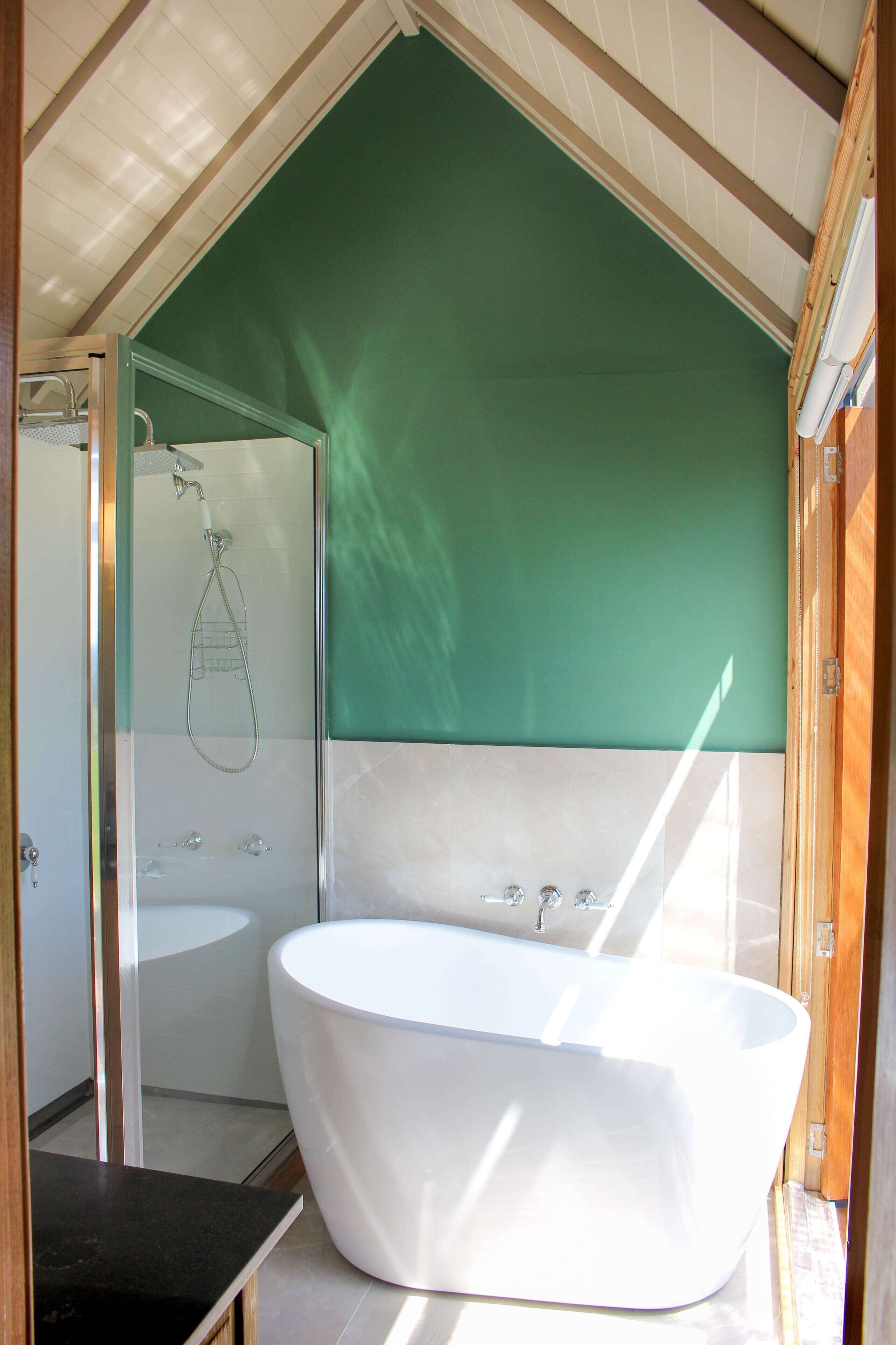 Un baño moderno con una bañera independiente, ducha con cerramiento de vidrio y una pared verde decorativa.