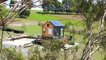 A small wooden cabin with a solar panel roof, surrounded by a gravel area and a wooden fence.
