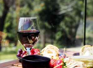 A wine glass filled with red wine, a bowl of strawberries, and a plate of cheese and crackers on a wooden table.