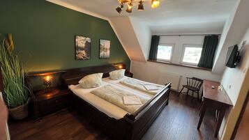 A bedroom with a wooden bed, a small desk, a chair, a radiator, and a window with curtains.