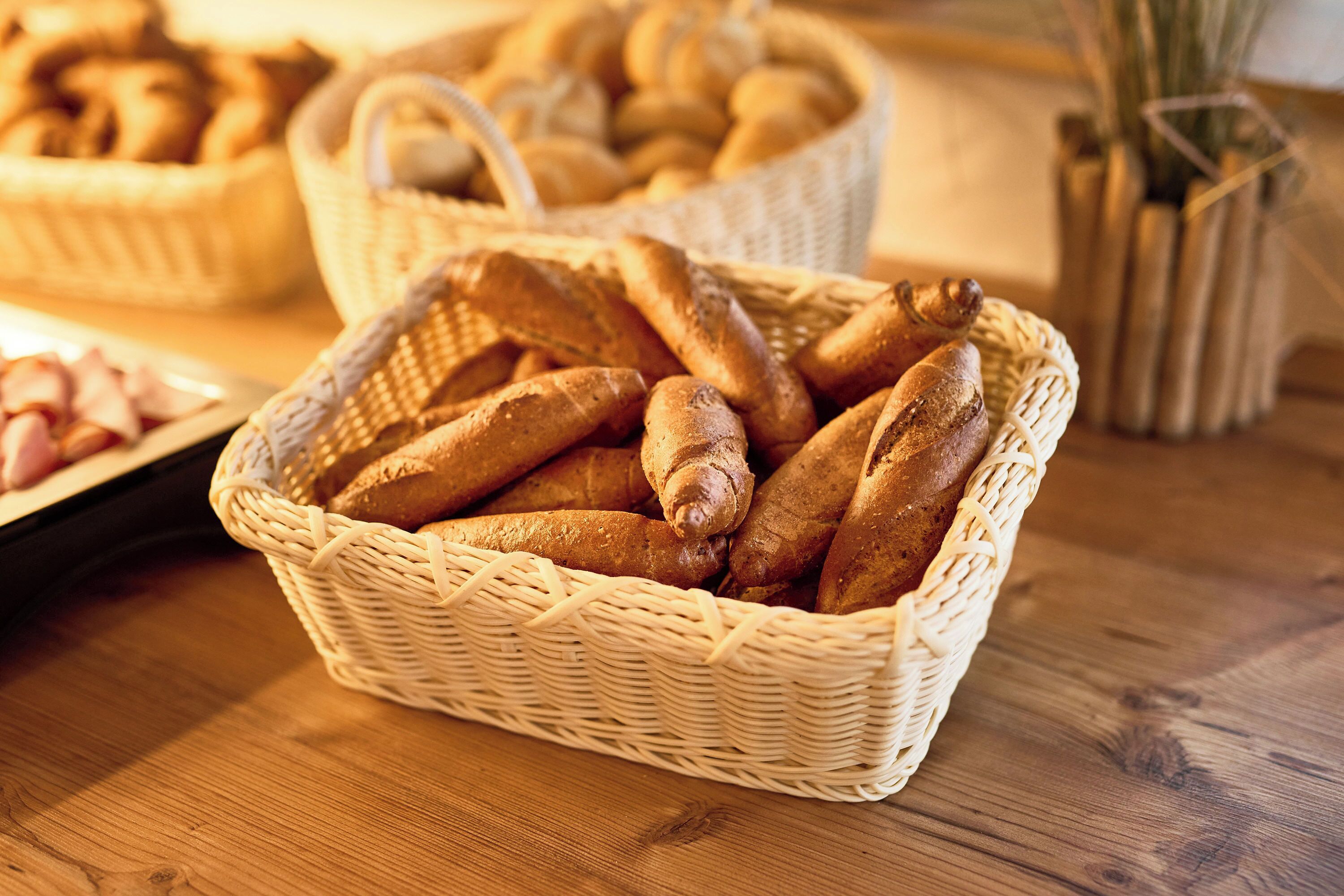 Een rieten mand gevuld met stokbroden op een houten tafel.
