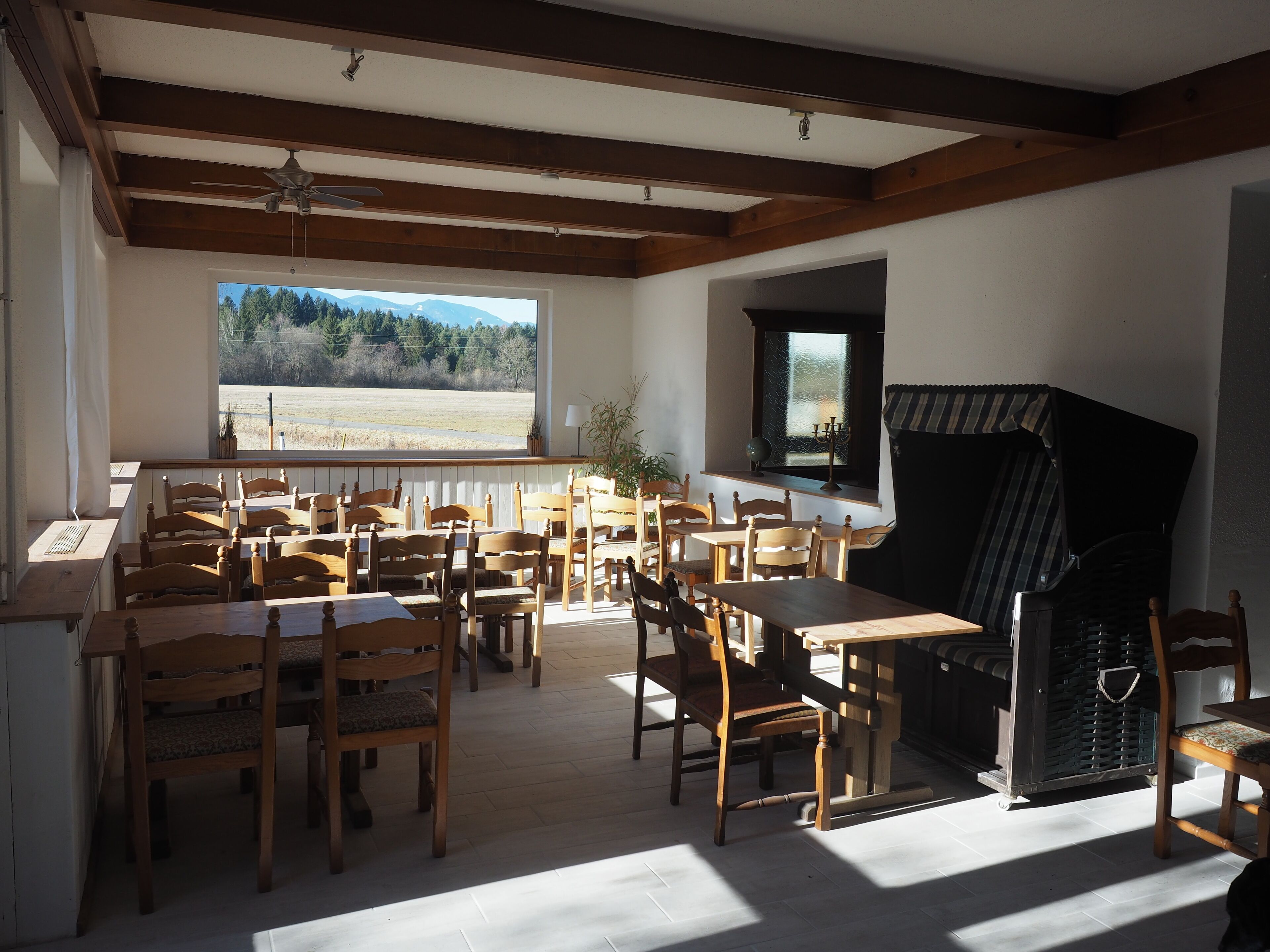 A dining area with wooden tables and chairs, a fireplace, and a view of a field through a large window.