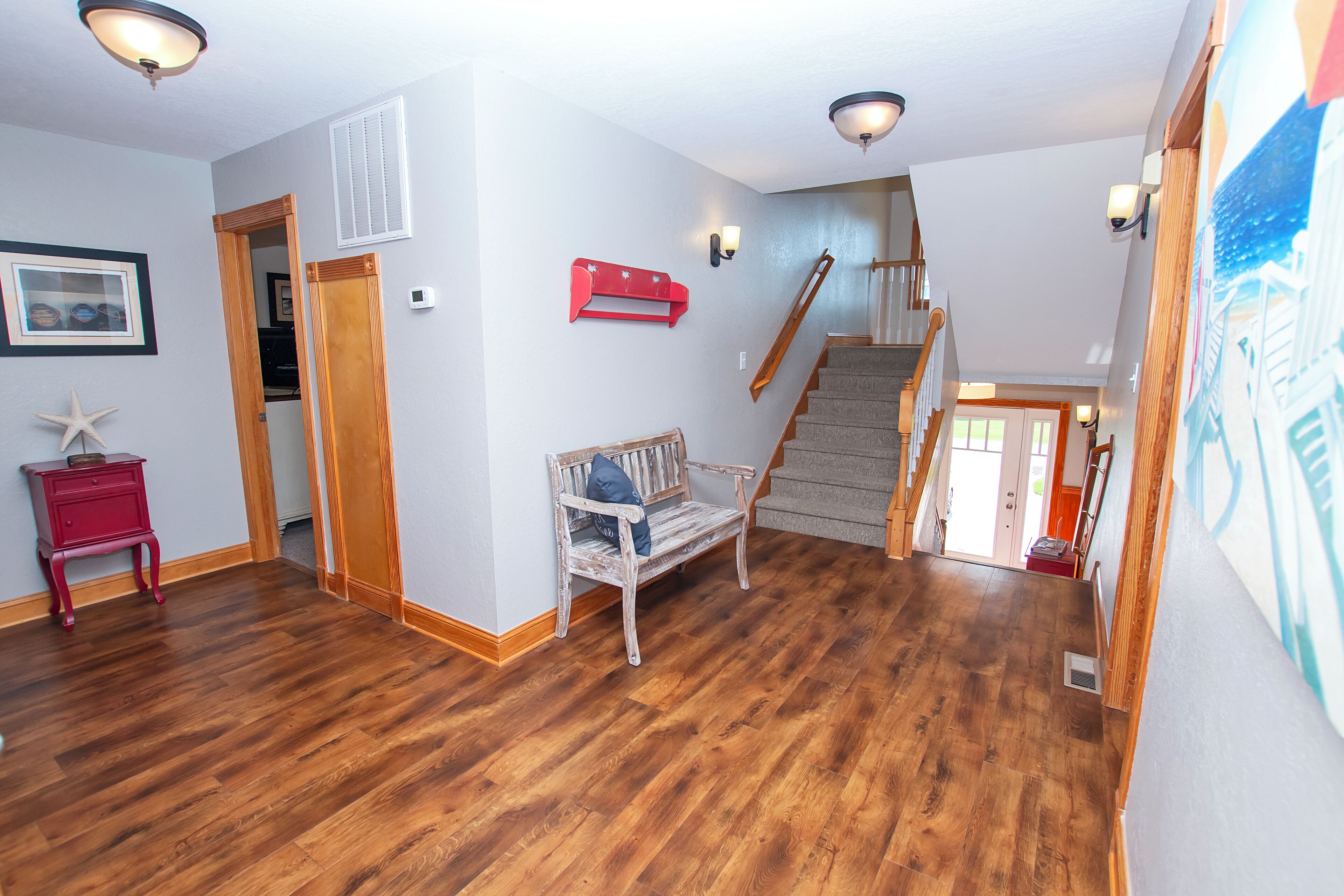 Un hall d’entrée spacieux, doté de planchers en bois, d ’un banc en bois, d’une table de chevet rouge et d’un escalier menant à un autre niveau.
