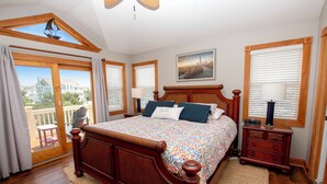 A bedroom with a large bed, wooden headboard, a nightstand, a lamp, and a view of a balcony. - Oceanside, 8 BRs, Private Pool and Hot Tub, Pool Table, PI109, Sweet TEA (Corolla)
