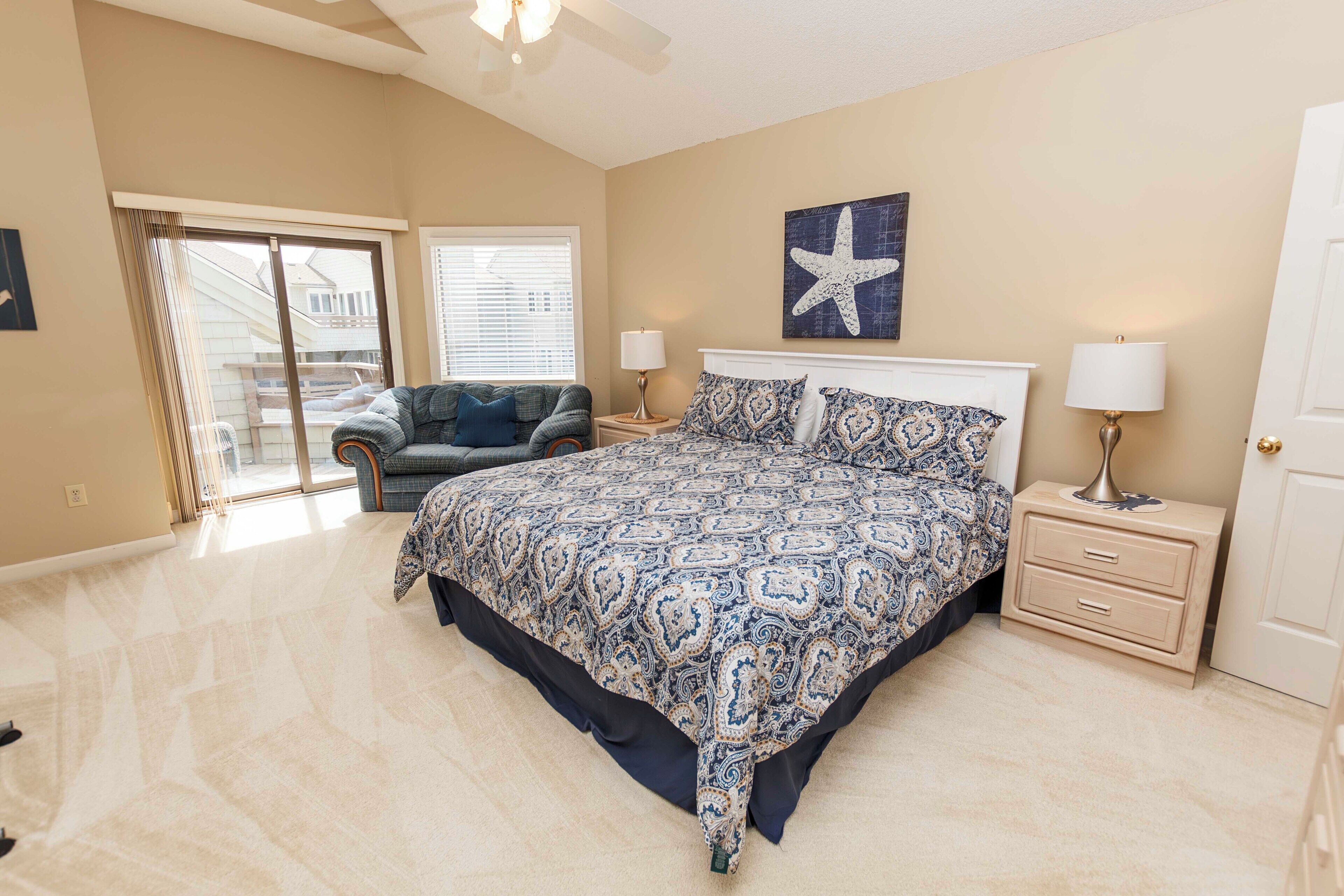 A bedroom with a large bed, two bedside tables with lamps, a starfish artwork on the wall, and a view through a sliding door to the outside.