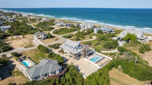 Oversigtsbillede af et kystnært boligområde med huse, en swimmingpool og en strand.