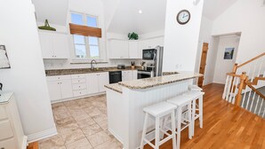 A modern kitchen with white cabinetry, a granite countertop, and a central island with bar stools. - Semi-Oceanfront, Private Pool with big pool deck, Close to Beach, PI12, A Shore Thing (Corolla)