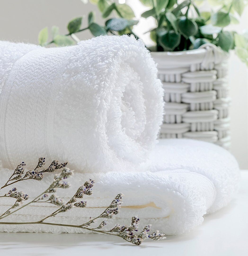 A neatly folded white towel with a plant and dried lavender in the background.