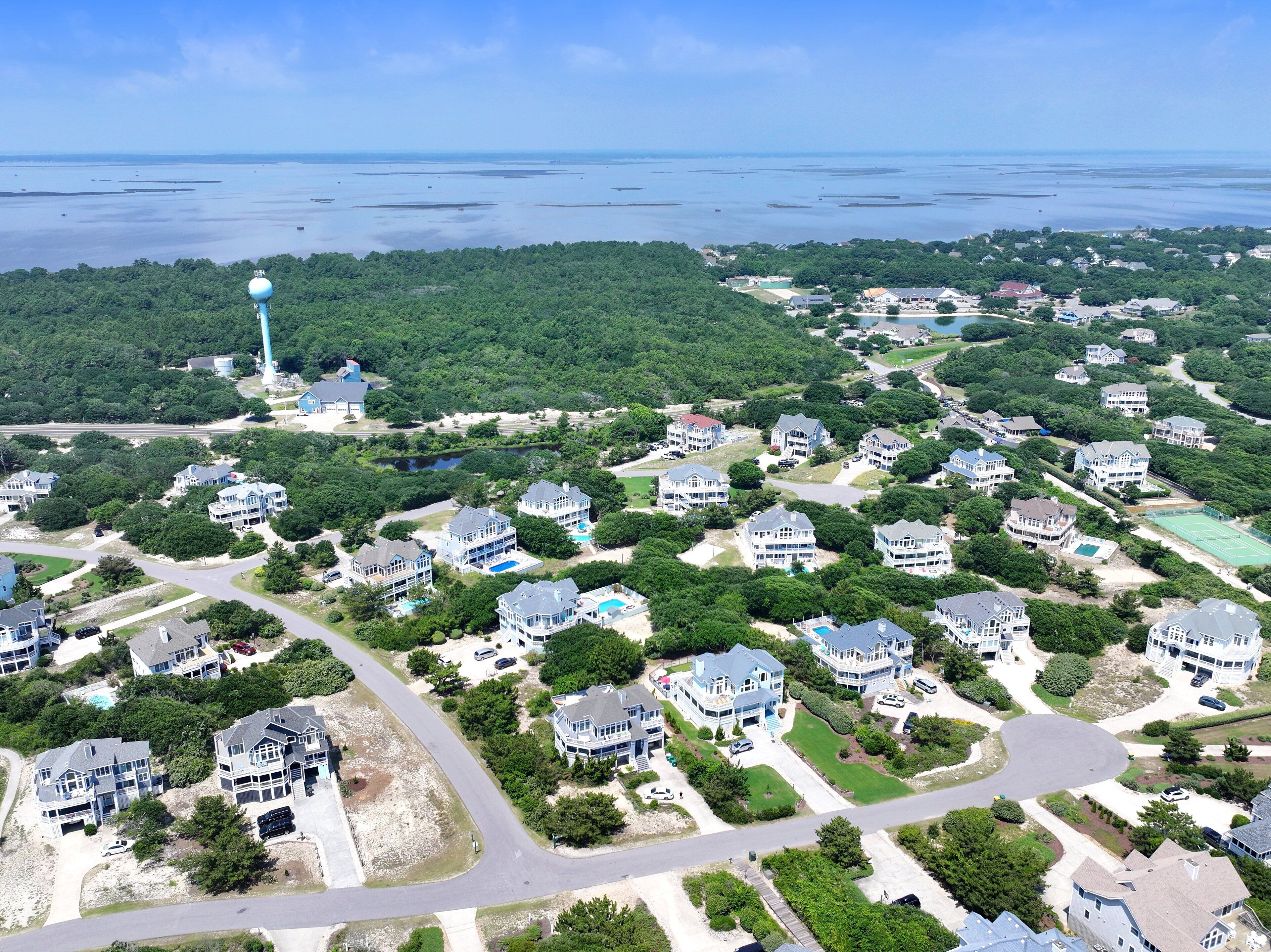 An aerial view of a coastal residential area with houses, roads, and a lighthouse.