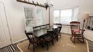A dining area with a wooden table and chairs, a chandelier, and large windows with blinds.