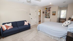 A bedroom with a blue sofa, a bed with striped bedding, a bookshelf, and a window with blinds.