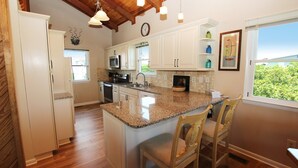 A kitchen with white cabinets, granite countertops, and a large island with bar stools. - Oceanside, Private Pool, Screened Porch, Close to Beach Access, OS3H, Brigadune (Corolla)