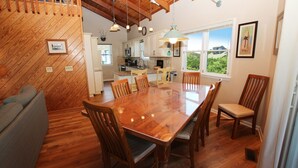 A dining area with a wooden table and chairs, a kitchen in the background, and a window with a view. - Oceanside, Private Pool, Screened Porch, Close to Beach Access, OS3H, Brigadune (Corolla)