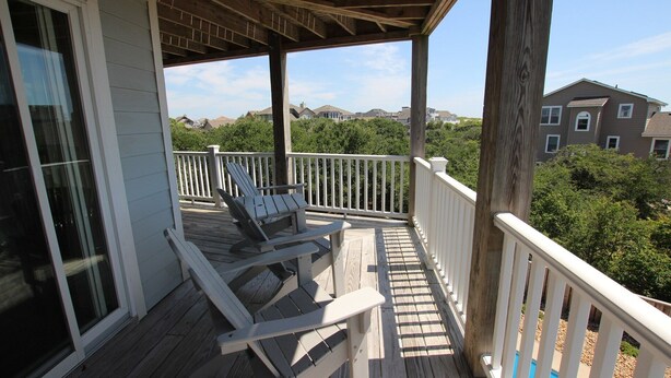 A wooden deck with two Adirondack chairs, a white railing, and a view of residential buildings and trees. - Oceanside, Private Pool, Screened Porch, Close to Beach Access, OS3H, Brigadune (Corolla)