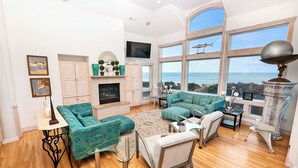 Un salon spacieux doté d’une cheminée, de grandes fenêtres et offrant une vue sur la mer.