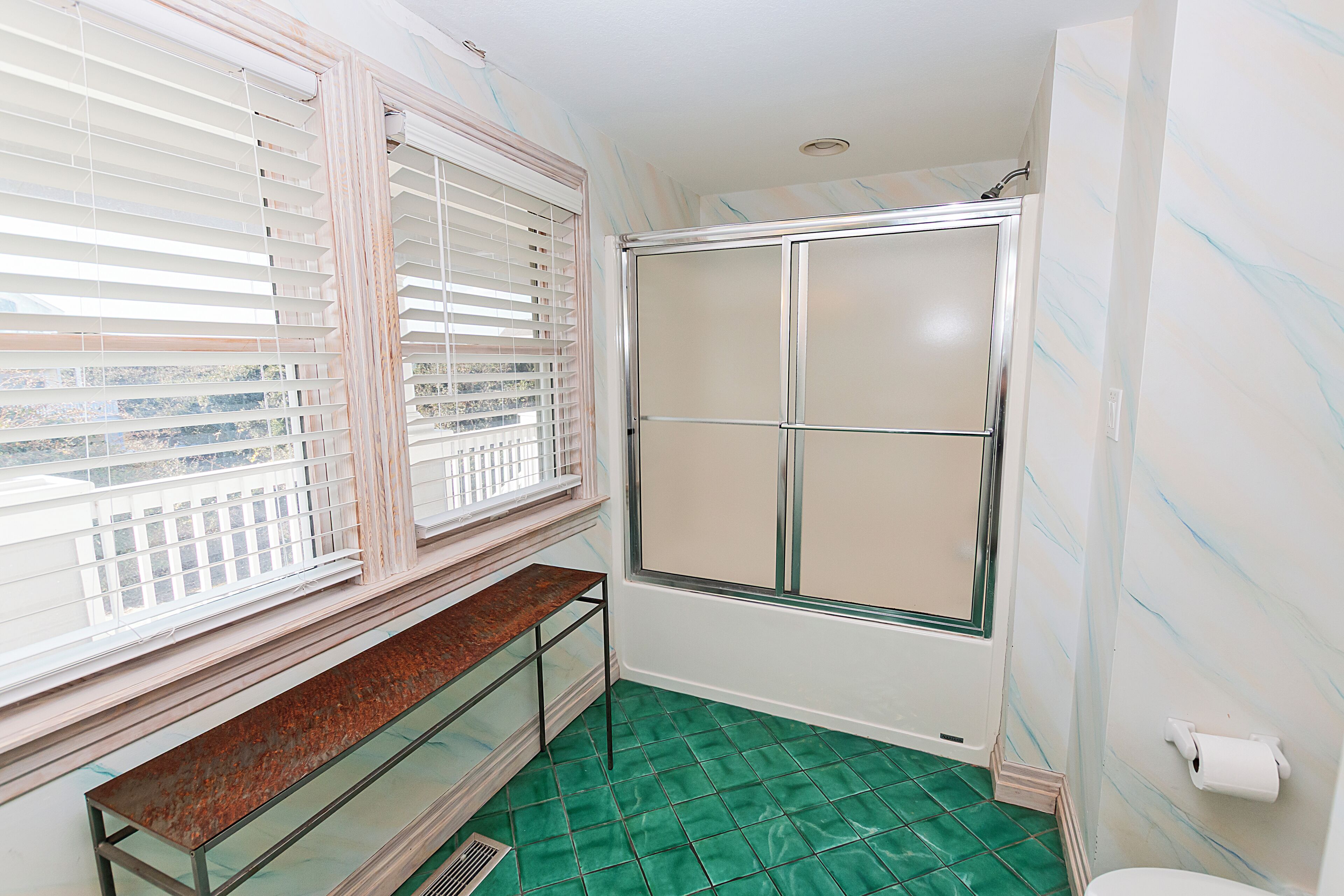 A bathroom with a shower, a toilet, and a window with blinds.