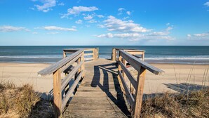 Une promenade en bois menant à une plage, avec un ciel dégagé.