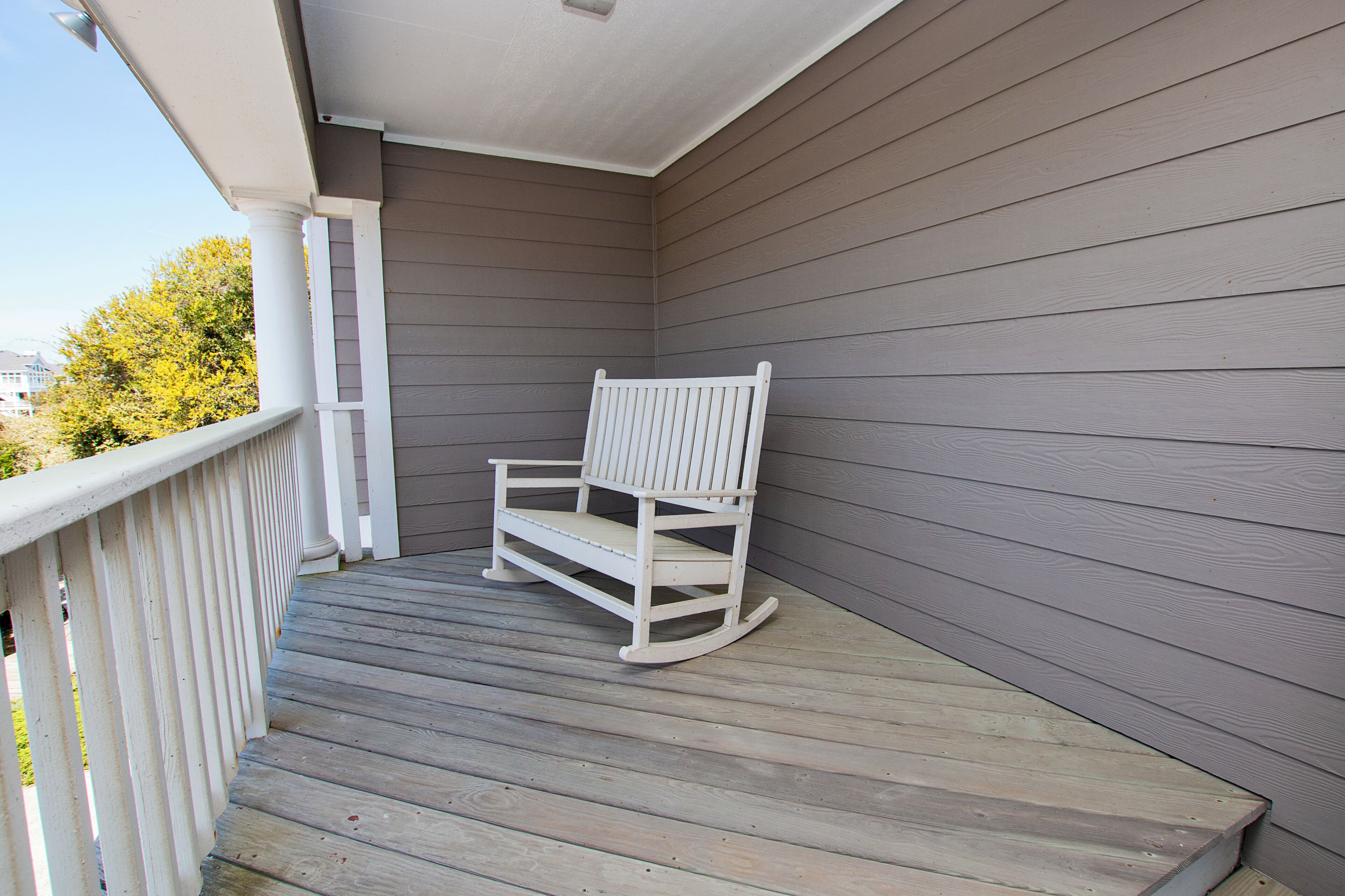 Une véranda en bois avec une chaise berçante et une balustrade blanche.