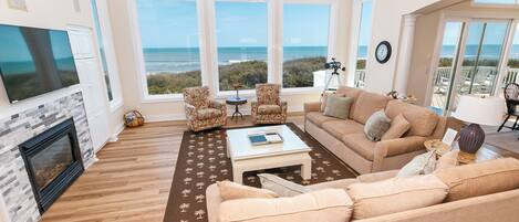 A spacious living room with a large window overlooking the ocean, a fireplace, and a cozy seating area.