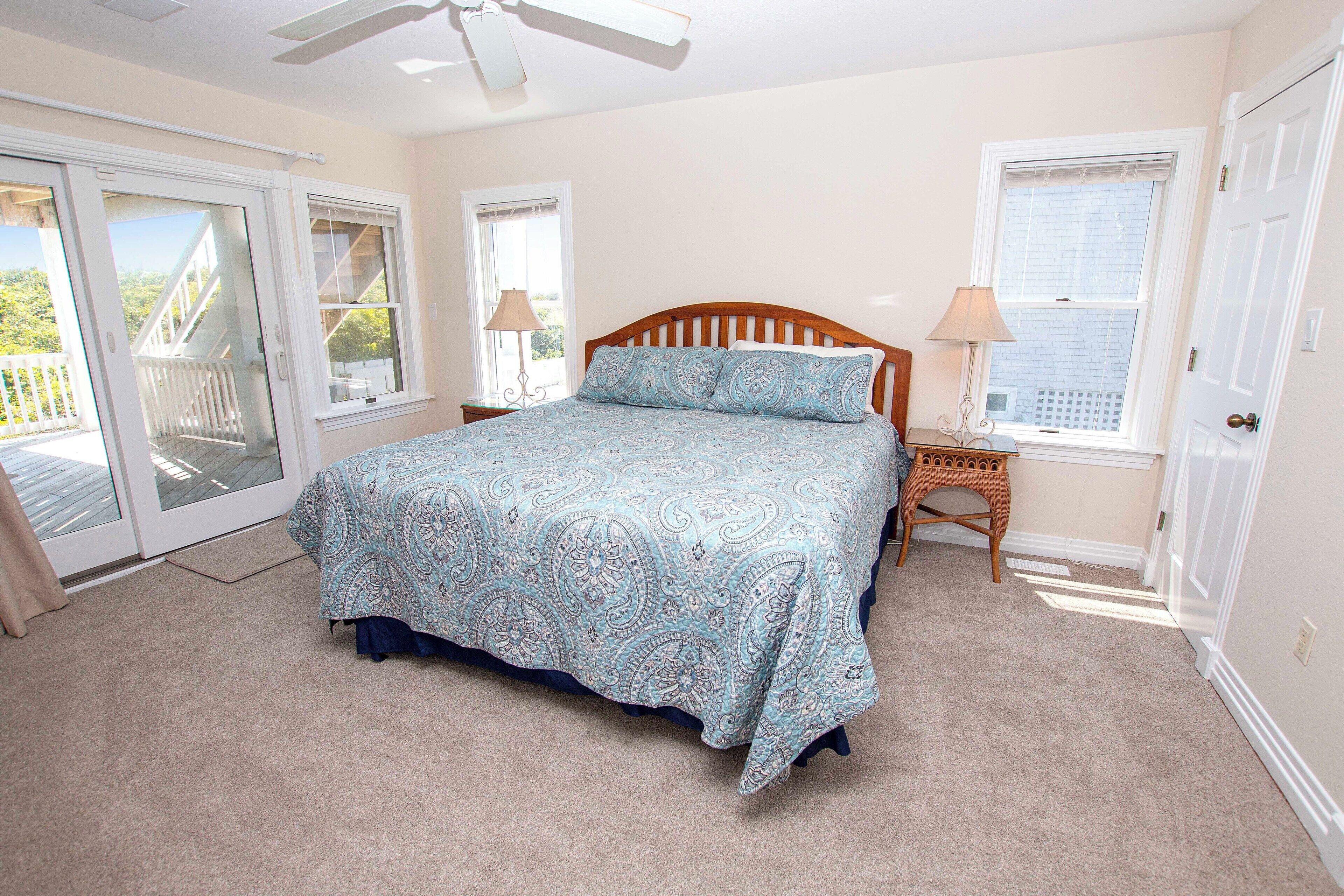 A bedroom with a bed, a nightstand, a lamp, a window, and a door.