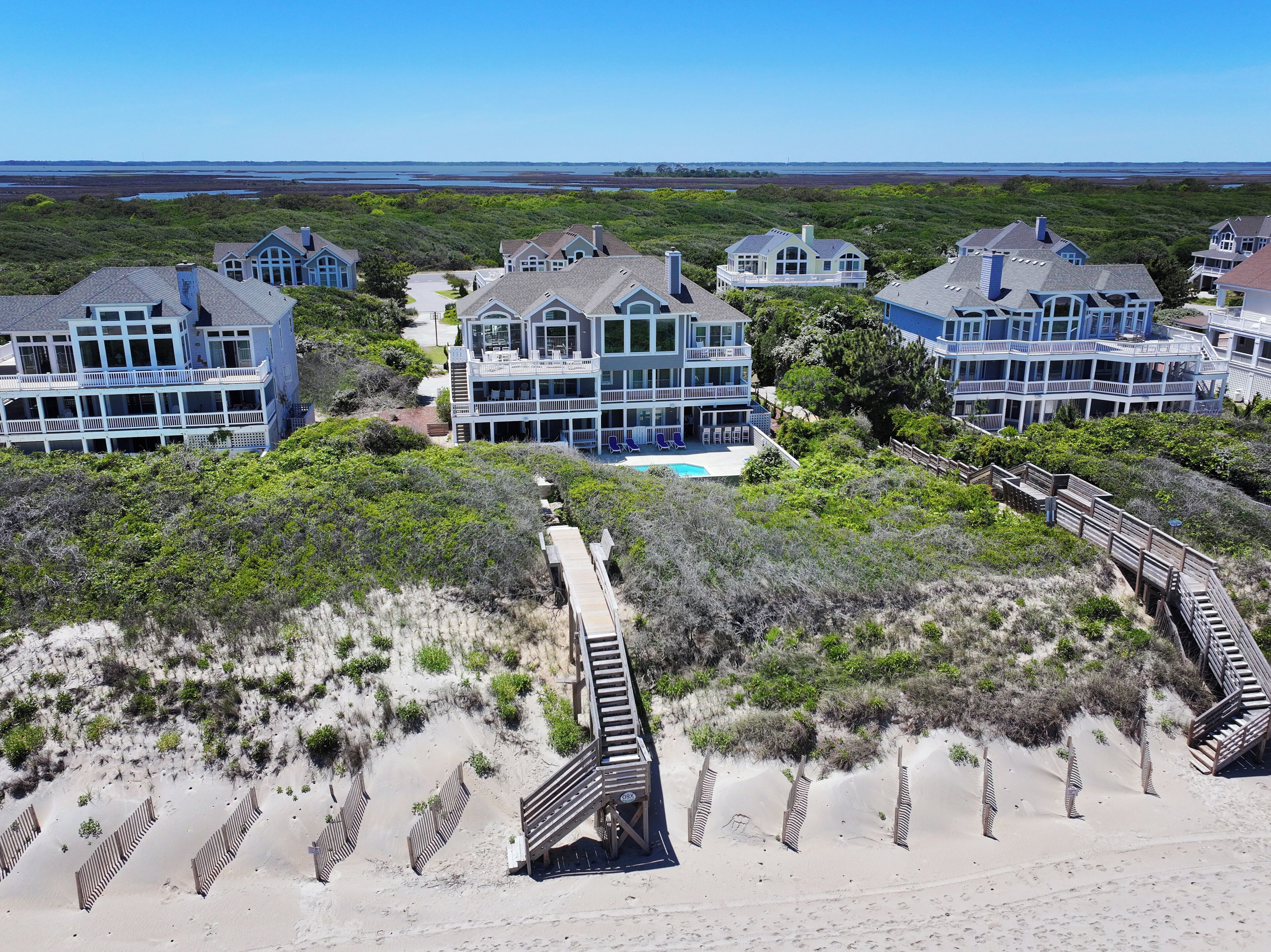 A beachfront property with multiple houses, a swimming pool, and a wooden boardwalk leading to the beach.