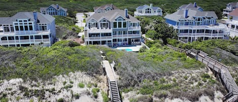 A beachfront property with multiple houses, a swimming pool, and a wooden boardwalk leading to the beach.
