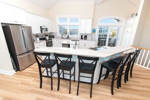 A modern kitchen with a central island, bar stools, and a view of the outside. - OCEANFRONT, Ocean Views, ELEV, Pool, Pool Table, Priv Beach Access, PI187, Right On The Beach (Corolla)