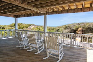 A wooden deck with white rocking chairs and a white railing overlooking a beach. - OCEANFRONT, Ocean Views, ELEV, Pool, Pool Table, Priv Beach Access, PI187, Right On The Beach (Corolla)