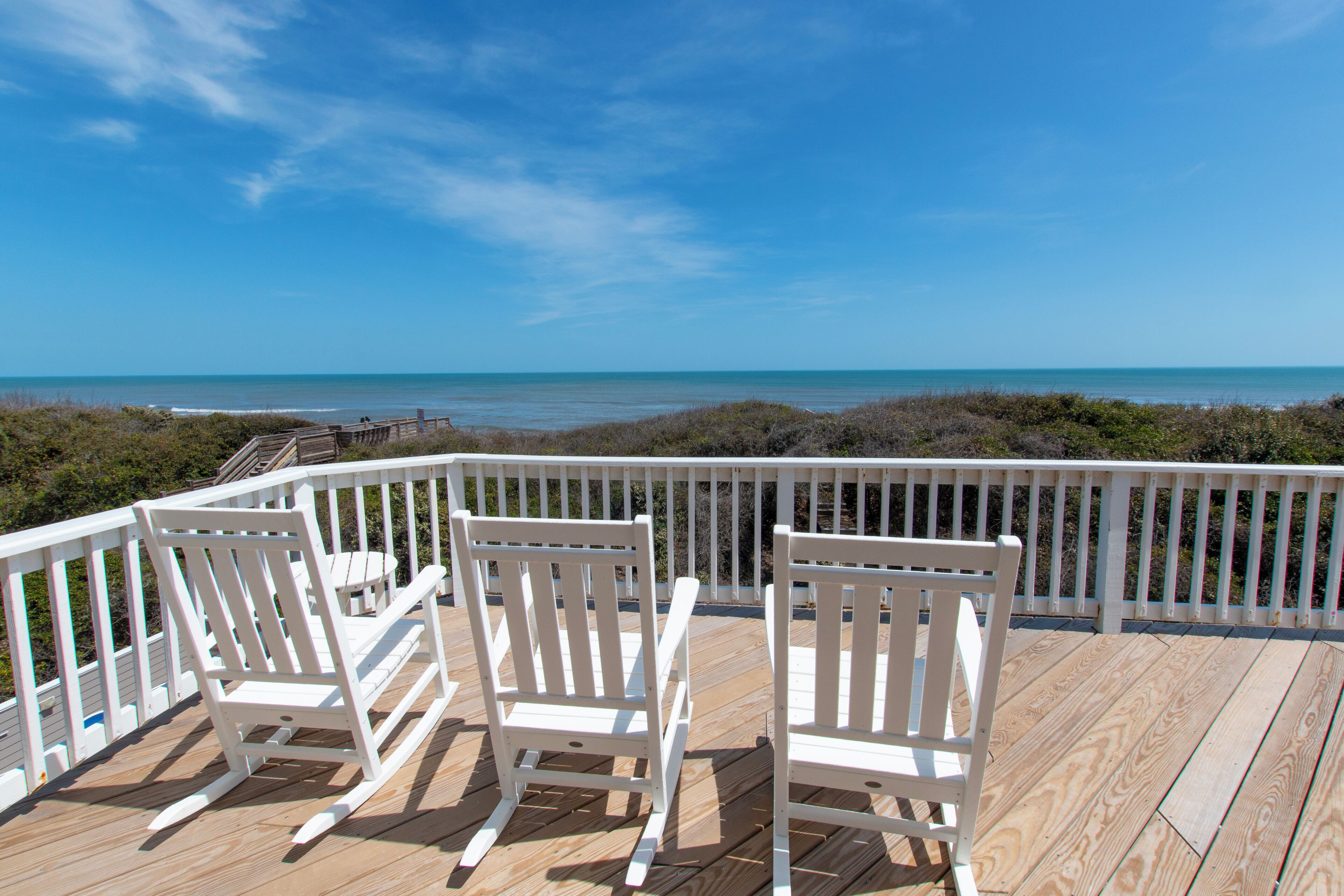 Een houten terras met witte relingen met uitzicht op een strand.