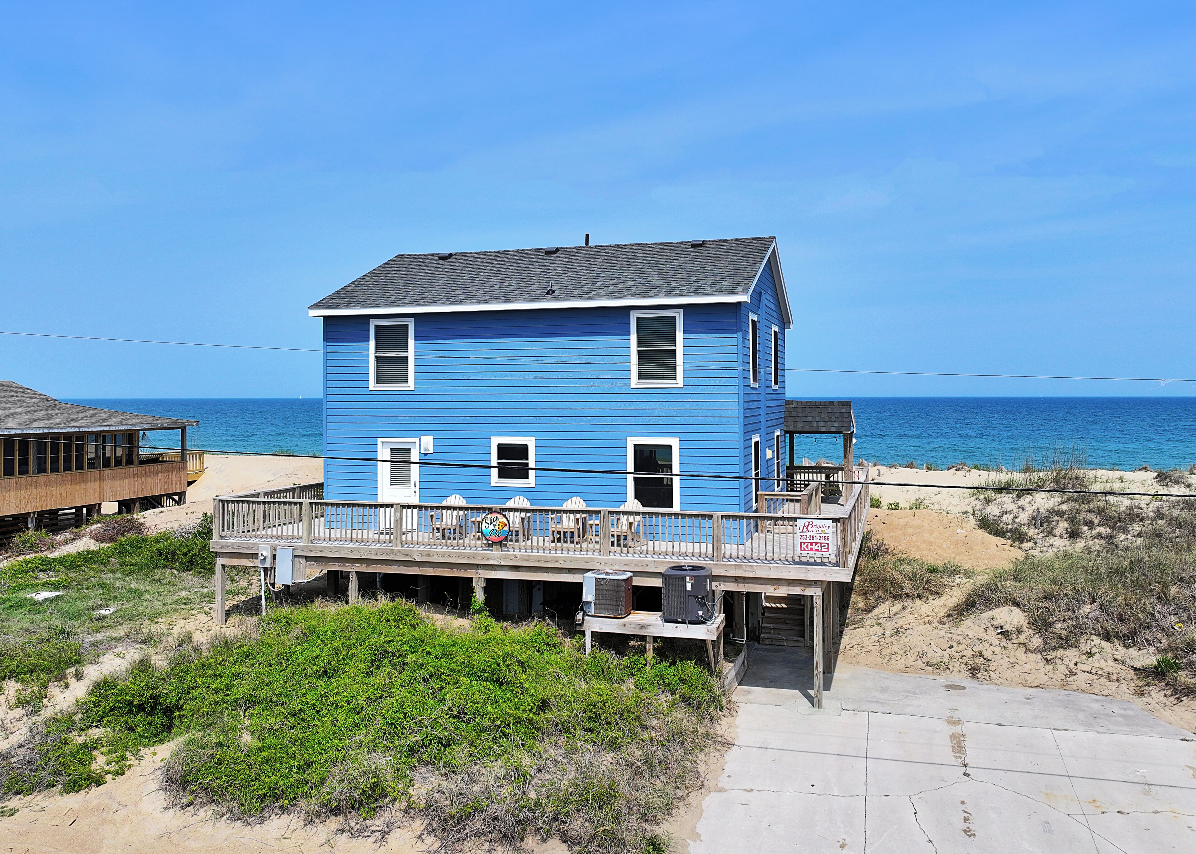 Une maison de plage à deux étages avec une terrasse, située près de l’océan.