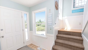 A staircase with carpeted steps leading to a landing, a white door, and a window with a view of greenery. - Oceanside, Private Pool, Hot Tub, ELEV, Close to Beach Access, OS1C, Here At Last (Corolla)