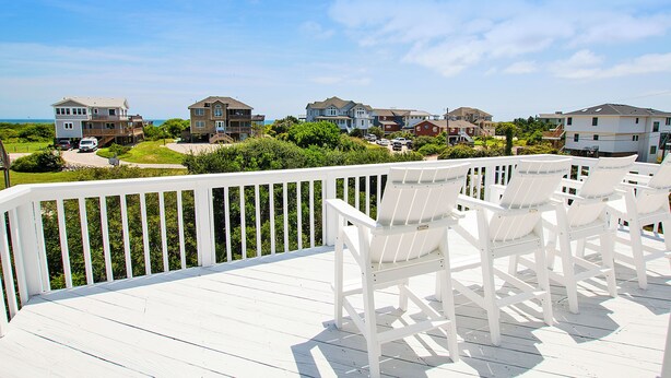 A deck with white railings and chairs, overlooking a residential area with houses and a clear sky. - Oceanside, Private Pool, Hot Tub, ELEV, Close to Beach Access, OS1C, Here At Last (Corolla)