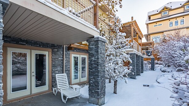 Un espacio exterior cubierto de nieve con un muro de piedra, una terraza de madera y un banco.