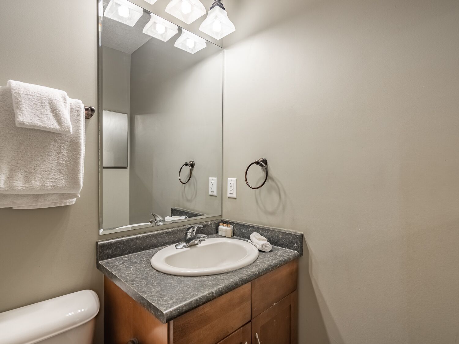 A bathroom with a white sink, a mirror, and two towel rings.