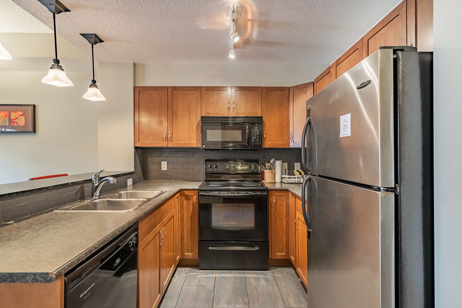 A modern kitchen with wooden cabinets, stainless steel appliances, a granite countertop, and pendant lighting.