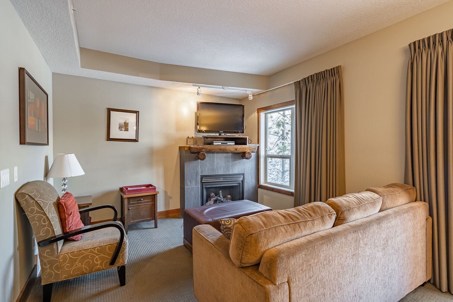 A cozy living room with a fireplace, a sofa, a chair, and a television.