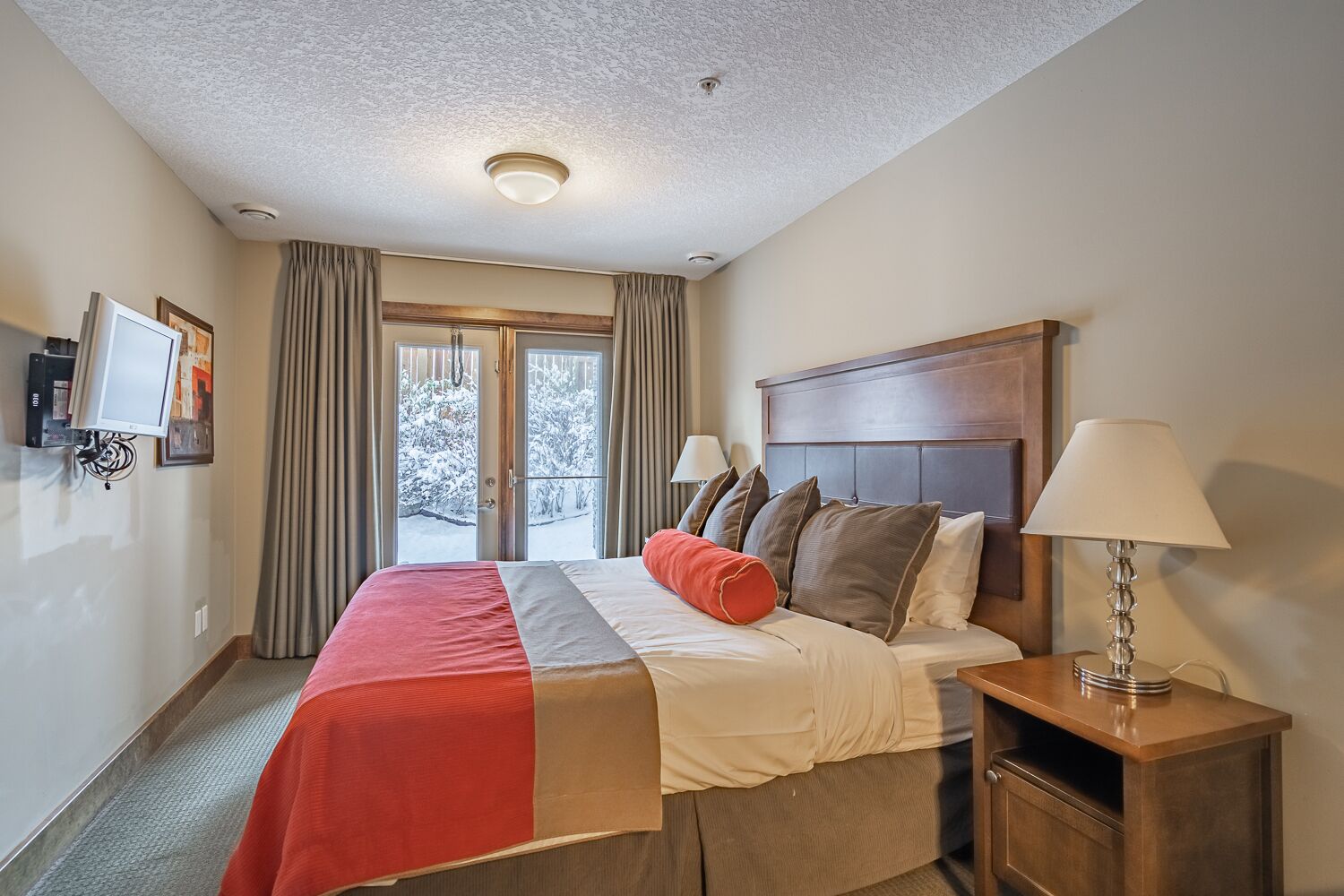 Une chambre d’hôtel avec un lit, une table de chevet, une lampe, une télévision et une vue sur l’extérieur.