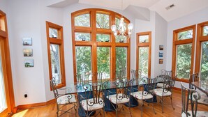 Zona pranzo con un tavolo grande e sedie, ampie finestre con vista sugli alberi e un lampadario.