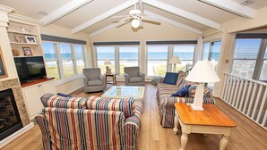 Un salón amplio con un ventanal que da a la playa, ventilador de techo y chimenea.