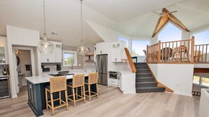 Una cocina amplia con una isla central, sillas de madera y una escalera que lleva a un nivel superior.