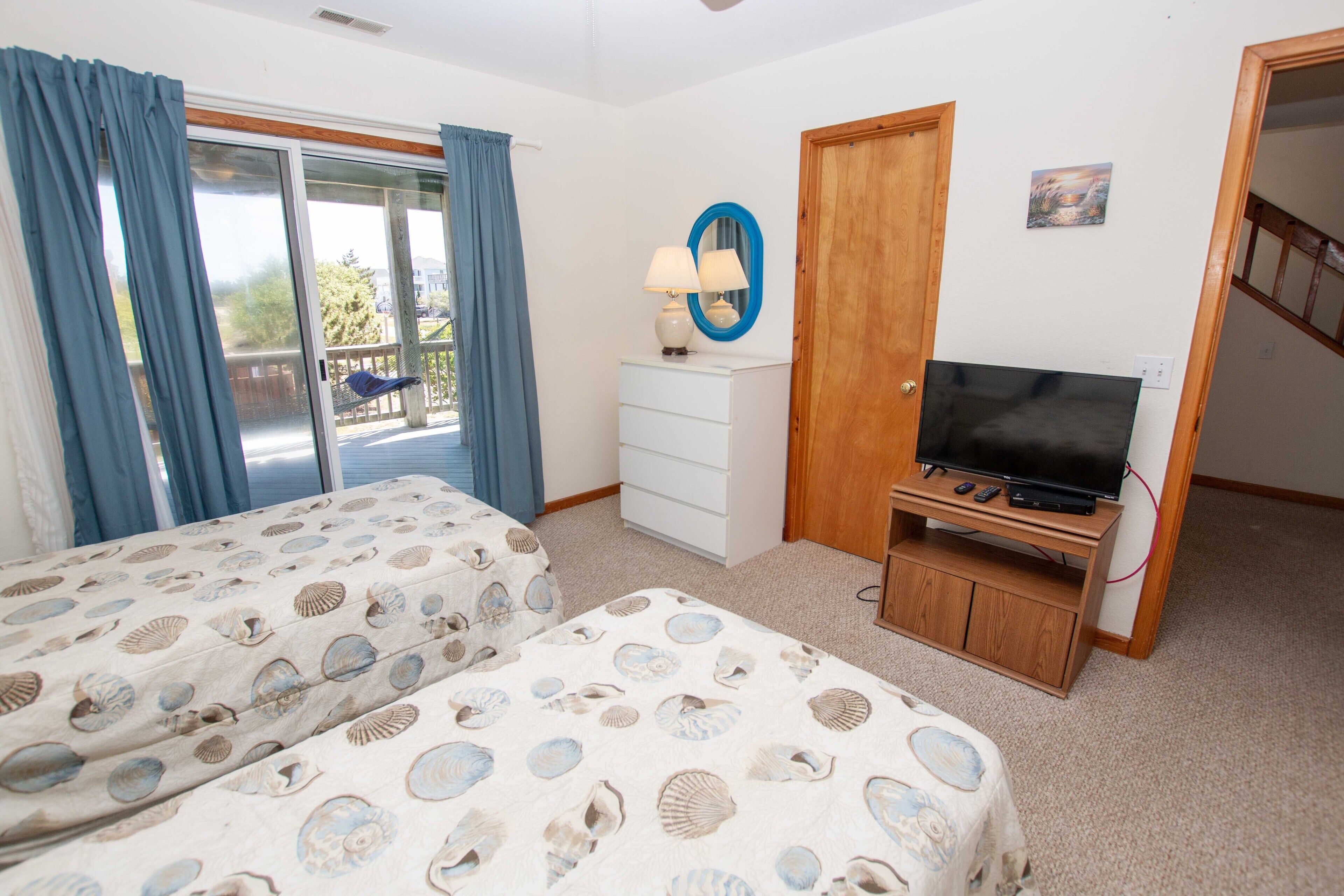 Une chambre avec deux lits, une télévision, une commode et une porte donnant sur un balcon.