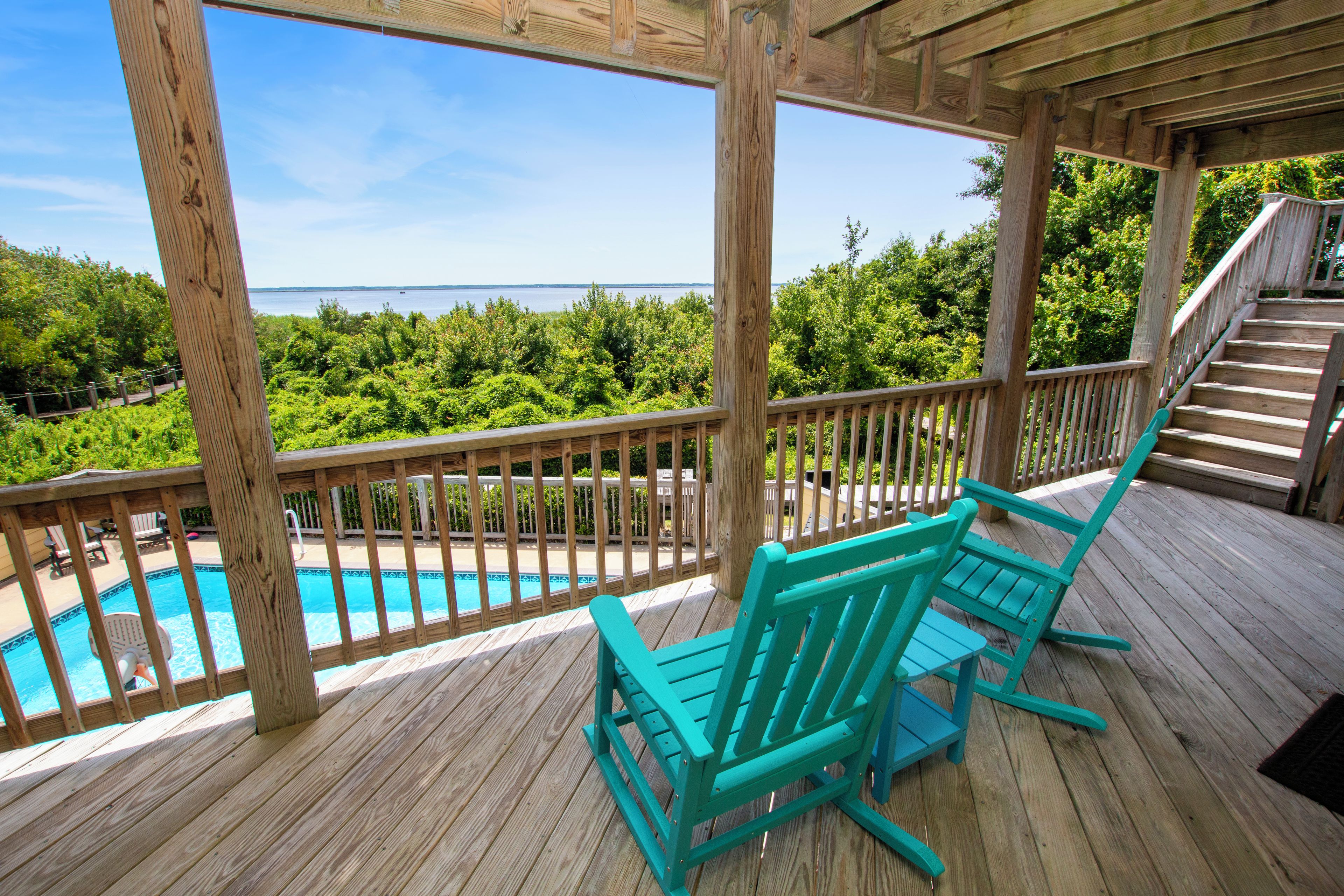 Une terrasse en bois avec une piscine, des chaises et une vue sur la mer.