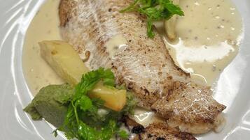A white plate with a piece of grilled fish, a slice of lemon, and a dollop of green sauce, garnished with parsley.