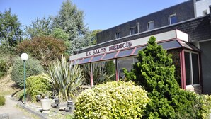 A building with a sign reading "LE SALON MEDICIS" surrounded by well-maintained greenery and a clear sky. - Henri 4 (Rostrenen)